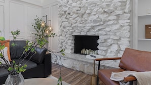 A modern living room with a stone fireplace, leather sofa, and a coffee table. - Backyard Oasis: Pool, Hot Tub, Giant Chess & Golf (Fort Worth)