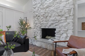 A modern living room with a stone fireplace, leather sofa, and a coffee table. - Backyard Oasis: Pool, Hot Tub, Giant Chess & Golf (Fort Worth)