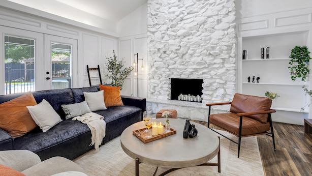 A modern living room with a stone fireplace, a dark blue sofa, a leather armchair, and a round coffee table. - Backyard Oasis: Pool, Hot Tub, Giant Chess & Golf (Fort Worth)