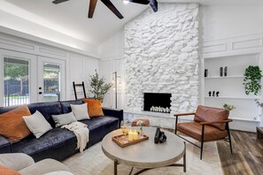 Un salon moderne avec une cheminée en pierre, un canapé bleu foncé, un fauteuil en cuir et une table basse ronde.