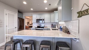 Una cocina moderna con una isla central, taburetes de bar, electrodomésticos de acero inoxidable y salpicadero.