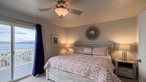 Un dormitorio con una cama grande, un ventilador de techo, vistas al exterior y una mesita de noche con lámpara.