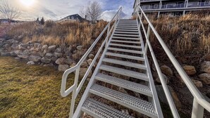 Una escalera metálica conduce a un edificio con varios balcones, rodeado de hierba seca y rocas.