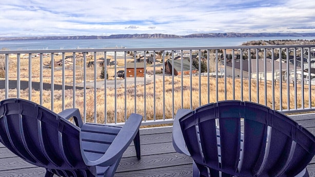 Un balcón con dos sillas que ofrece vistas panorámicas a una playa y montañas a lo lejos.
