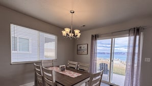 Un comedor con una mesa, sillas, una araña y un ventanal con persianas, con vista al exterior.