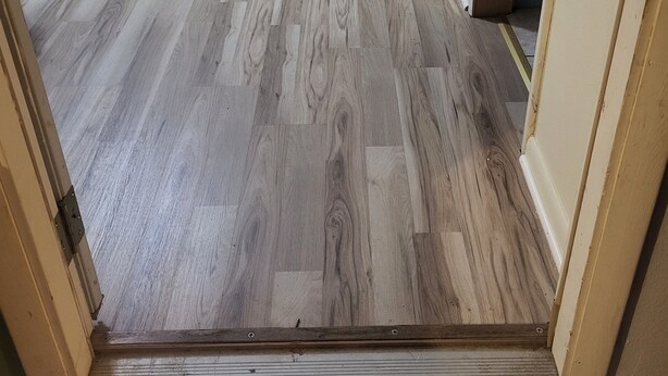 Una habitación con piso de madera, un escritorio con computadora y una estantería.