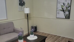 Una sala de estar con una mesa de centro de madera oscura, un sofá gris, una lámpara de pie y dos cuadros colgados en la pared.