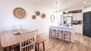 A modern kitchen with a wooden dining table, white chairs, and a bar area with stools.