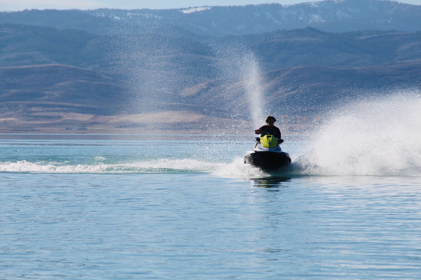 A person jet-skiing on a lake with mountains in the background.