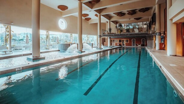 En inomhuspool med tydliga banor, stora pelare och utsikt över staden genom stora fönster.