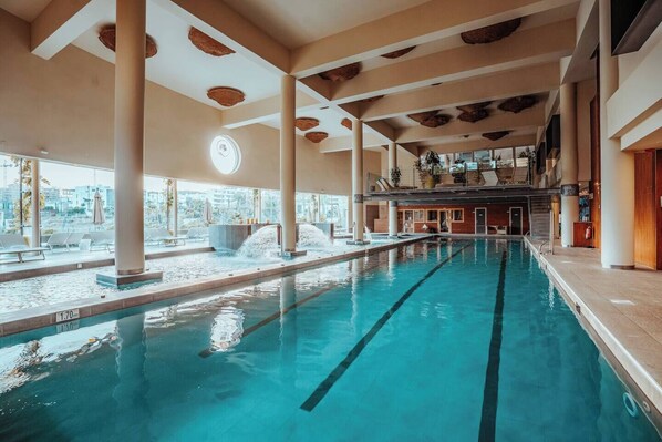 An indoor swimming pool with clear lanes, large pillars, and a view of the city through large windows.