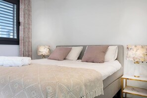 A neatly made bed with a patterned throw, a bedside lamp, and a wall-mounted lamp.