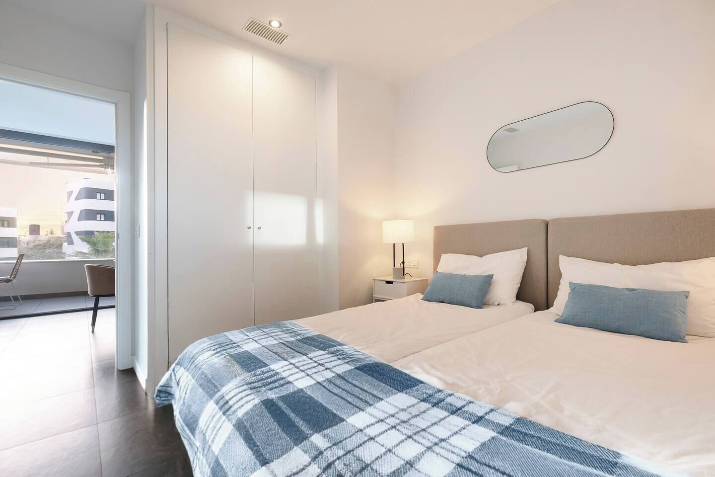 Una habitación de hotel con cama, una mesita de noche con lámpara, una ventana y vistas a edificios.