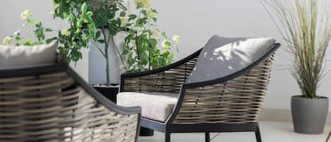 A wicker chair with a cushion, positioned on a tiled patio with potted plants.