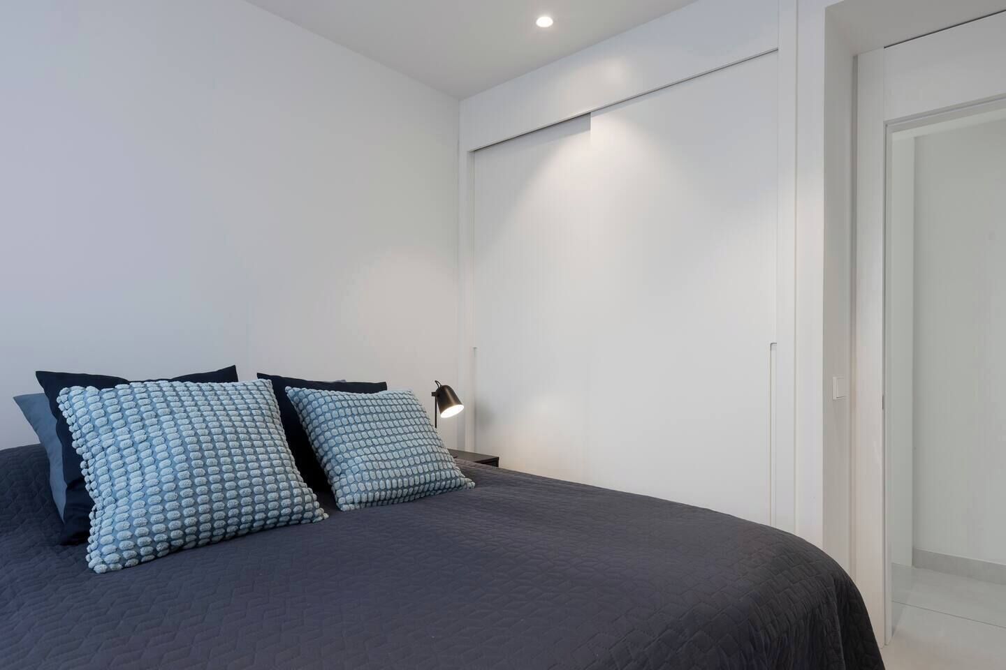A bedroom with a bed, two pillows, a bedside lamp, and a door.