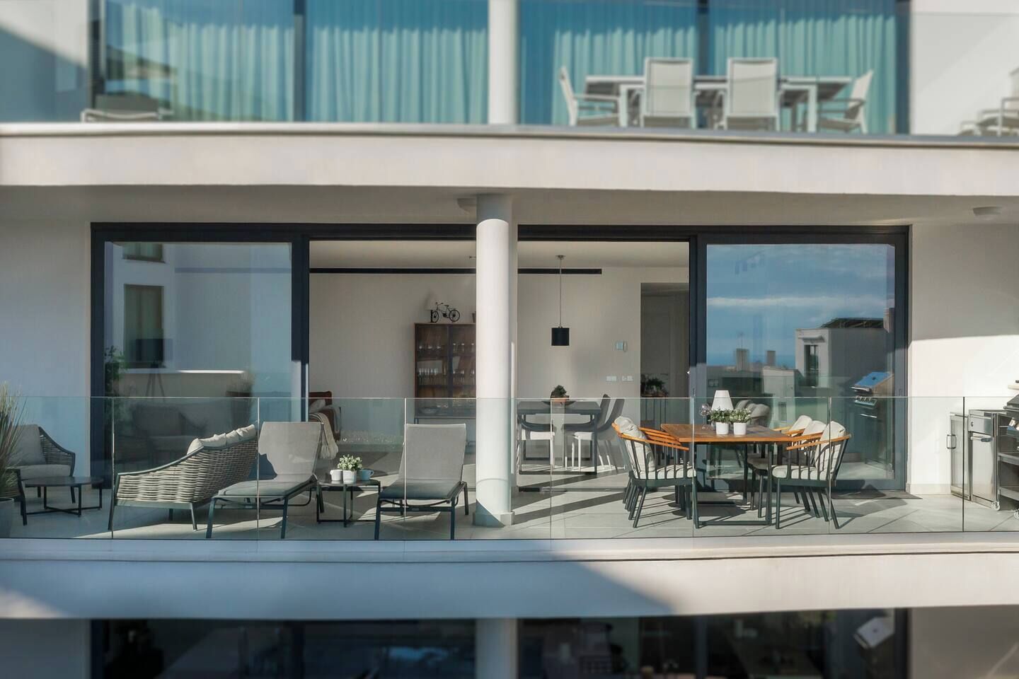 Een modern appartement met een balkon, ingericht met rieten stoelen en een eettafel.