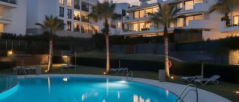 Ett modernt hotell med en swimmingpool, palmer och solstolar.
