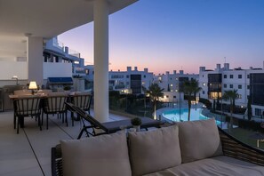 A balcony with a dining area, a sofa, and a view of a swimming pool and buildings. - Luxury 3-Bedroom Apartment in Higuerón (La Capellania)