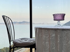 Une table recouverte d’une nappe en dentelle, un saladier en verre violet et une chaise avec un coussin.