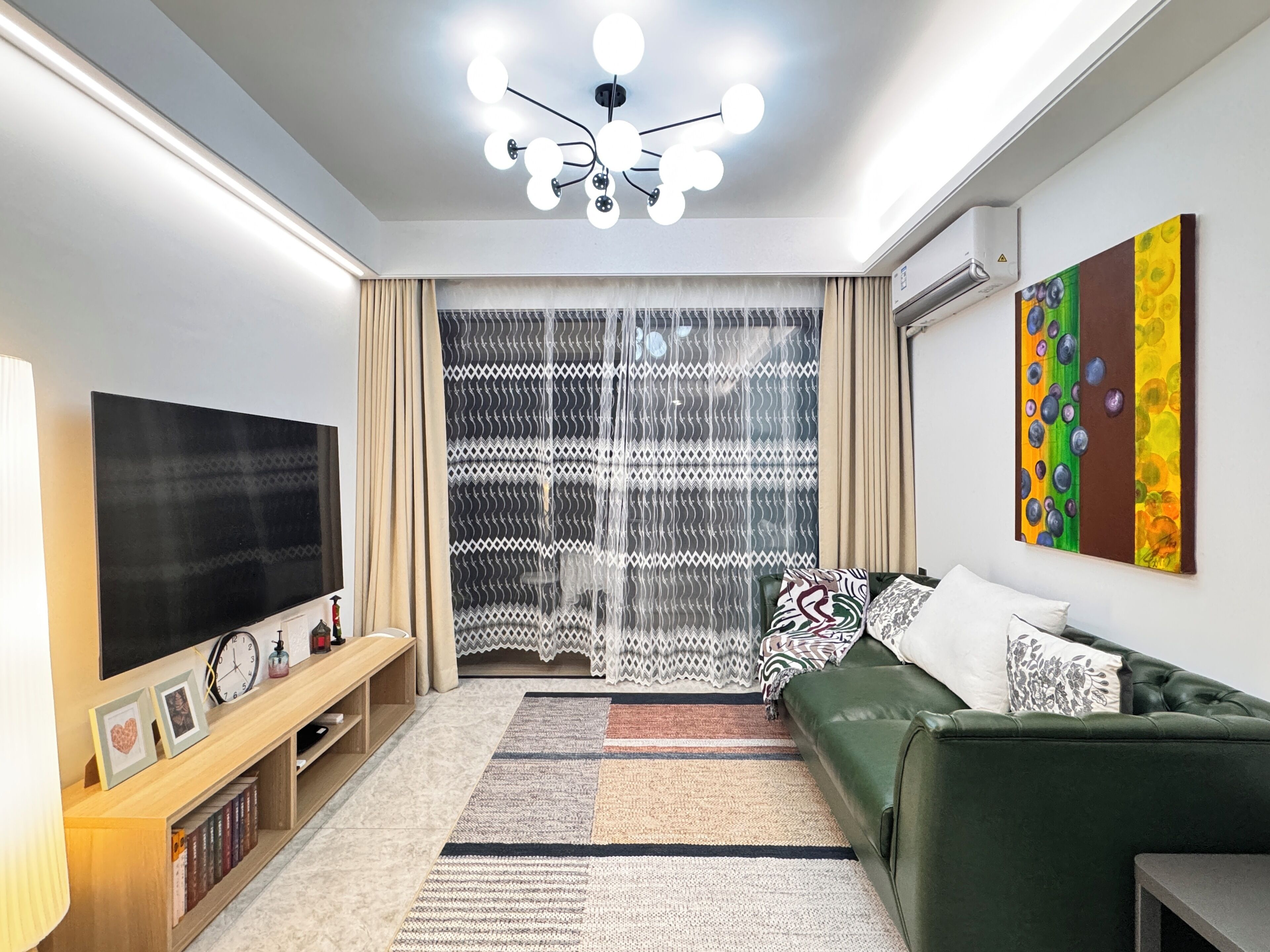 Una sala de estar moderna con un televisor de pantalla plana, un sofá verde, un tapete estampado y una lámpara en el techo.