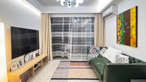 A modern living room with a flat-screen TV, a green sofa, a patterned rug, and a ceiling light fixture.