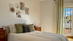 A bedroom with a large bed, a nightstand, a dresser, and a window with curtains.