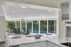 Eine moderne Küche mit einer großen Kochinsel, Essbereich und Blick auf einen Swimmingpool.