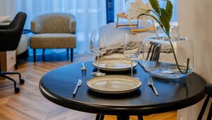 Un coin repas avec une table ronde dressée pour deux personnes, une chaise, un petit canapé et une plante en pot.