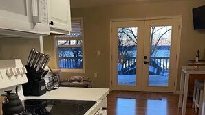 A kitchen with a stove, microwave, and cabinets, a dining area with a table and chairs, and a view of a deck through a glass door. - Cayuga Lake Cottage near Aurora - Wineries, Brewery, Trails and Lakefront. (Aurora)