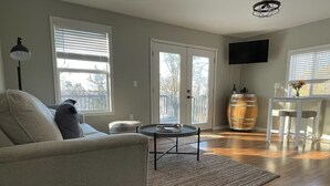 A living room with a sofa, a coffee table, a TV, and a wooden barrel. - Cayuga Lake Cottage near Aurora - Wineries, Brewery, Trails and Lakefront. (Aurora)