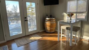 Une pièce avec un plancher en bois, une table blanche avec deux chaises, un tonneau en bois et un téléviseur fixé au mur.