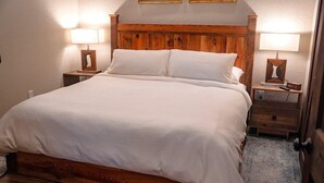 Un lit bien fait, avec une tête de lit en bois, deux tables de chevet avec des lampes et une petite table de nuit en bois, également avec une lampe.