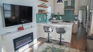 A modern kitchen with a TV, bar stools, and a fireplace. - Deluxe Two-Bedroom, Two-Story Resort Cabin (Bronson)