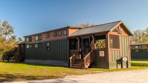 A two-story building with a porch, a staircase, and a small attached structure. - Deluxe Two-Bedroom, Two-Story Resort Cabin (Bronson)
