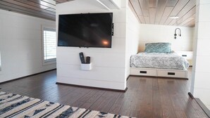 A modern room with a flat-screen TV mounted on a white wall, a bed with a patterned bedspread, and a small bedside table with a lamp. - Deluxe Two-Bedroom, Two-Story Resort Cabin (Bronson)