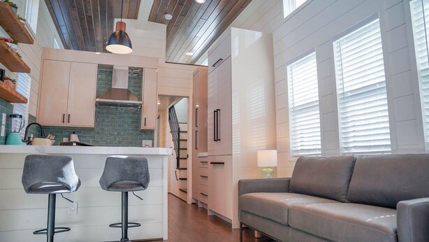 A modern kitchen with a central island, bar stools, a sofa, and a staircase leading to another level. - Deluxe Two-Bedroom, Two-Story Resort Cabin (Bronson)
