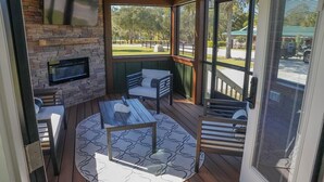 A covered outdoor seating area with a stone wall, a flat-screen TV, and a view of the outdoors. - Deluxe Two-Bedroom, Two-Story Resort Cabin (Bronson)