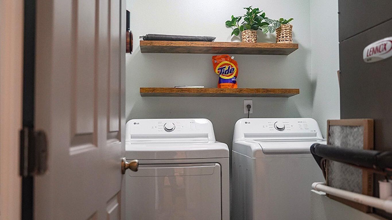 A laundry area with two white washing machines, a shelf with a Tide detergent bag, and a Lenox appliance on the wall.