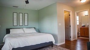 A bedroom with a bed, a door leading to a bathroom, and a hallway with a mirror.