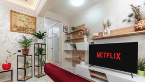 A modern living room with a large flat-screen TV, a red carpet, and various plants on shelves and tables. - Mina Home minutes from City Center and beach (Agadir)
