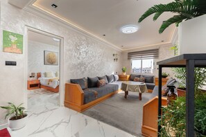 A modern living room with a sofa, a coffee table, and a dining area. There is a bed in the background and a staircase leading to an upper level. - Mina Home minutes from City Center and beach (Agadir)