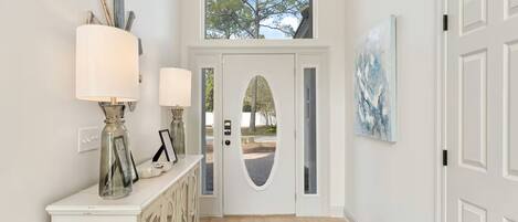 A hallway with a white door, a console table with lamps, and a painting on the wall.