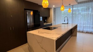 Una cocina moderna con una isla de mármol, armarios oscuros e iluminación colgante.