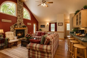 Una sala de estar acogedora con chimenea, un conjunto de sofás, un comedor con taburetes y una cocina con armarios de madera.