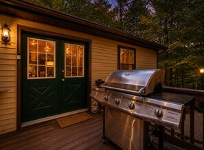 Una terraza de madera con una parrilla y una puerta verde con ventanas.