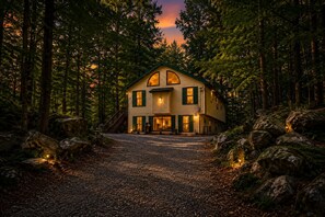 Una casa de dos pisos con un porche, rodeada de un bosque.