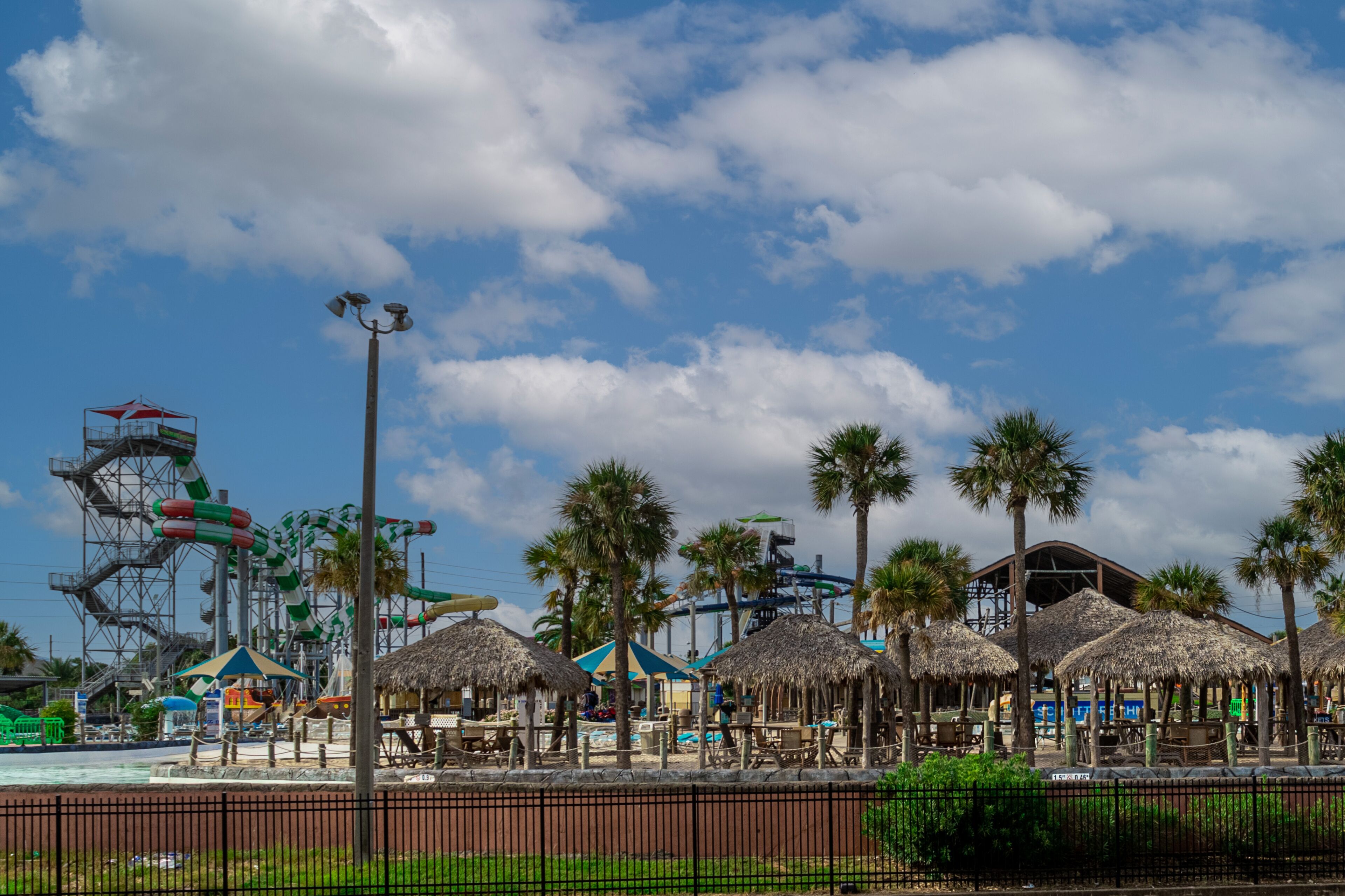A water park with a wave pool, palm trees, and thatched-roof structures.