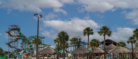 A water park with a wave pool, palm trees, and thatched-roof structures.
