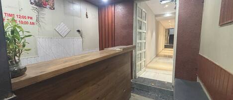 Un'area reception con una scrivania in legno, una ventola a soffitto, una sveglia a parete e una scala che conduce a un altro piano.