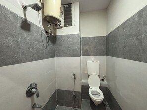 A small, tiled bathroom with a toilet, a shower, and a hand dryer mounted on the wall. - The Samsara Hotel (Indore)